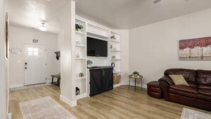 Un salon moderne avec un canapé en cuir marron, une bibliothèque intégrée blanche, une petite table ronde et un téléviseur à écran plat.