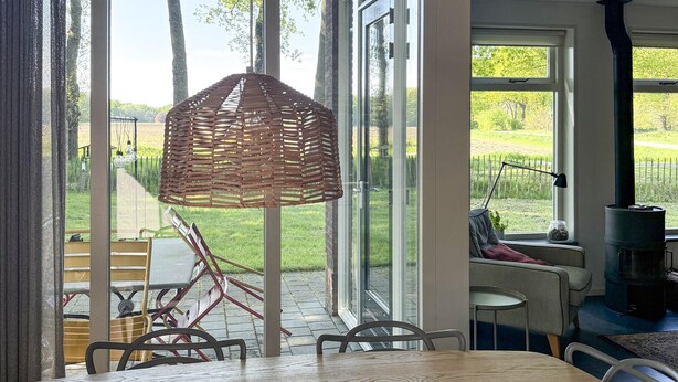 A dining area with a table and chairs, a wicker lamp, and a view of a garden through large windows. - 3 bedroom beautiful home in Gees (Gees)