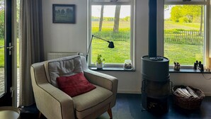 A cozy room with a sofa, a fireplace, and large windows offering a view of a green field. - 3 bedroom beautiful home in Gees (Gees)