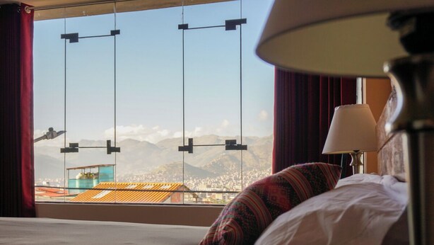 A hotel room with a bed, a window with a view of mountains, and a lamp. - Tradición: Studio apartment with a wonderful view, close to San Blas market (Cusco)