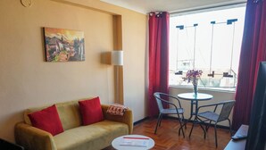 A room with a sofa, a small round table, a chair, a lamp, and a painting on the wall. - Tradición: Studio apartment with a wonderful view, close to San Blas market (Cusco)