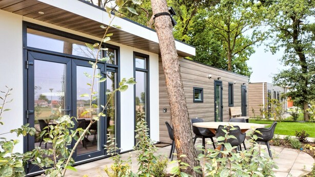 A modern house with large windows, a patio with outdoor furniture, and a tree in the foreground. - 2 bedroom cozy home in Hellendoorn (Hellendoorn)