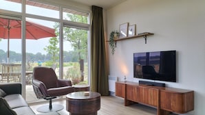 A modern living room with a large TV, comfortable seating, and a view of the outdoors. - 2 bedroom cozy home in Hellendoorn (Hellendoorn)