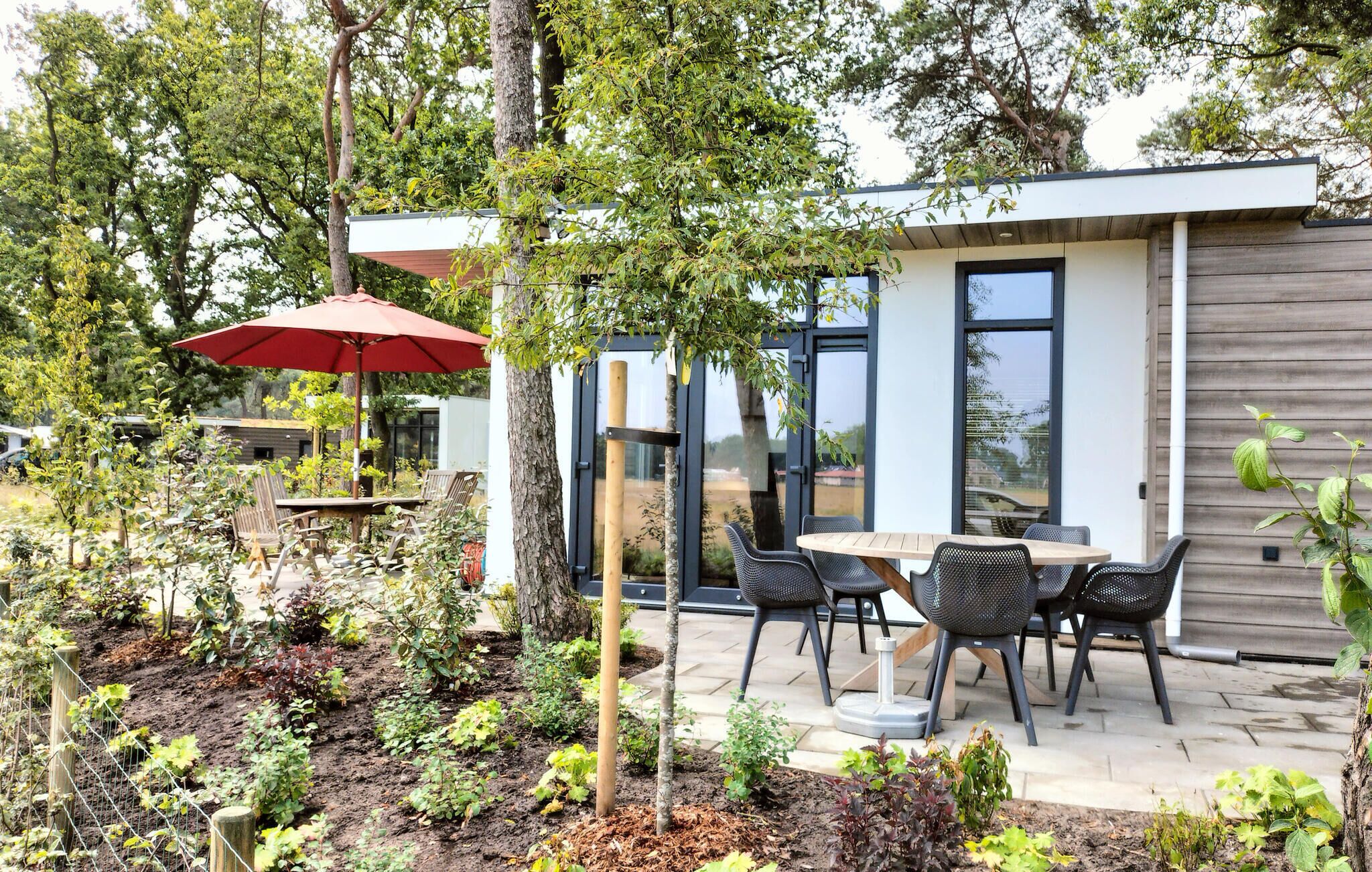 Une terrasse extérieure moderne, dotée d’une table et de chaises, et entourée d’une végétation luxuriante et d’arbres.