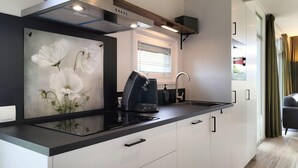 A modern kitchen with a black countertop, white cabinets, a stainless steel range hood, and a window with blinds.
