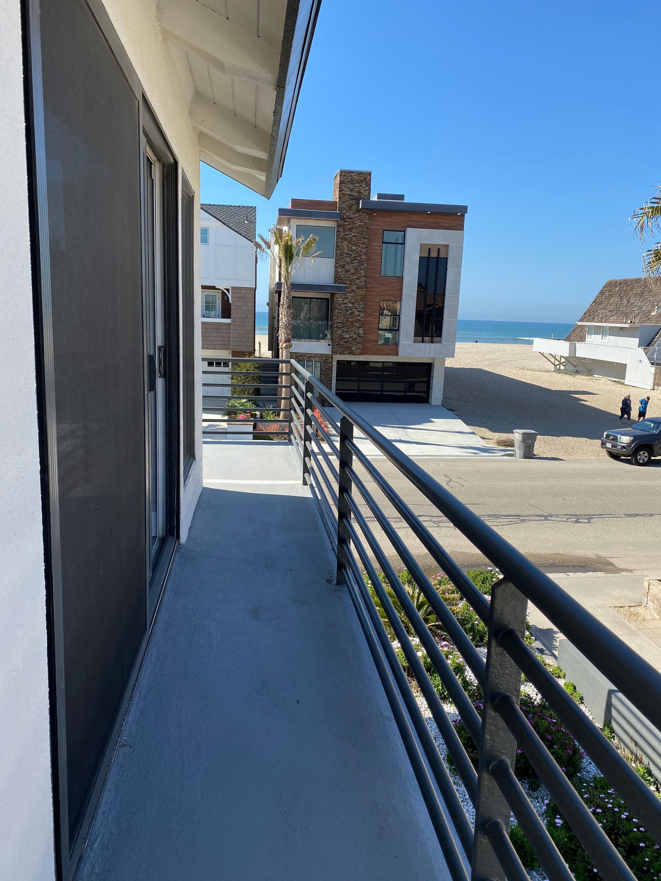 A balcony with a view of a modern building, a beach, and a parked car.