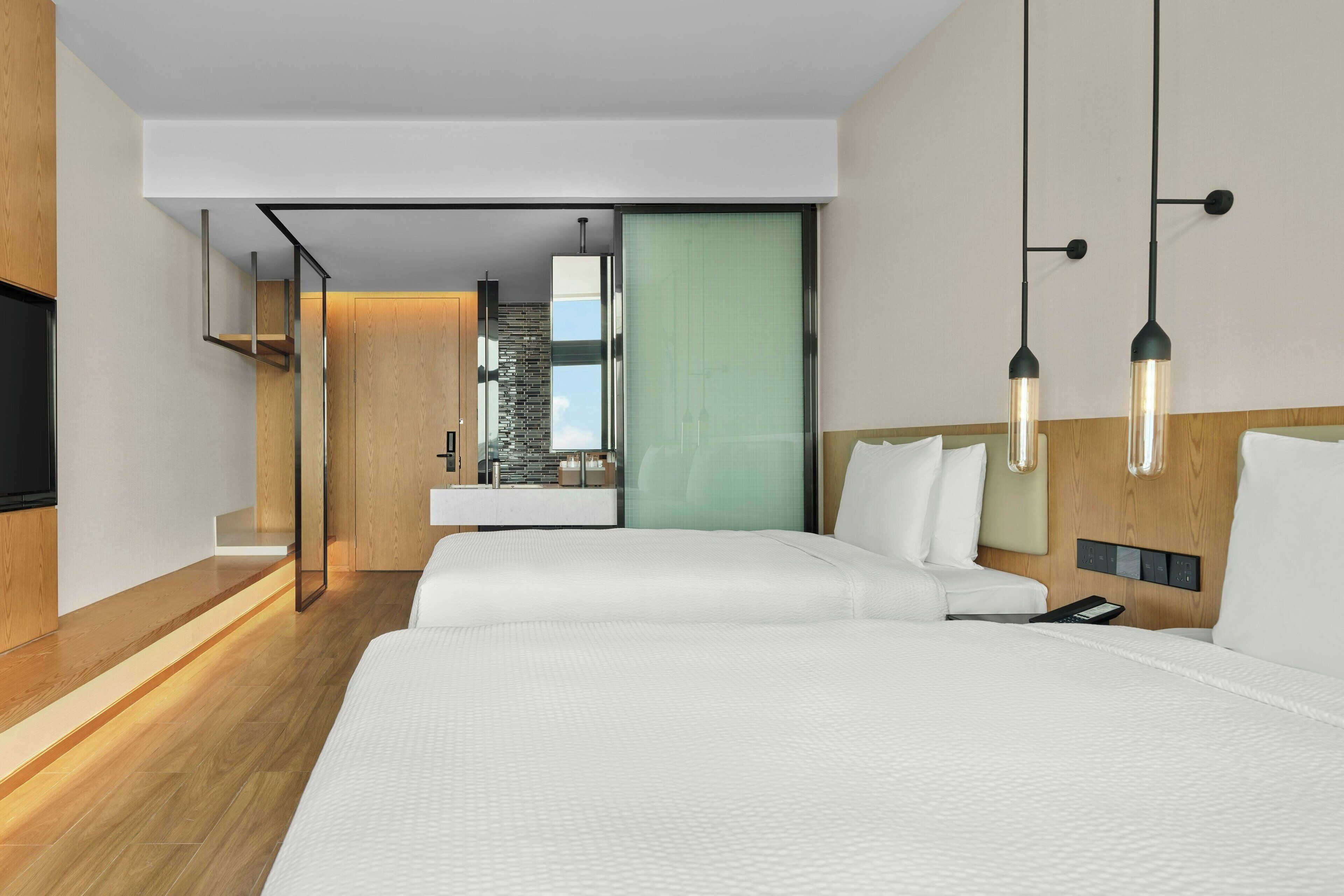 A modern hotel room with a large bed, a TV, a desk with a computer, and a view of the city.