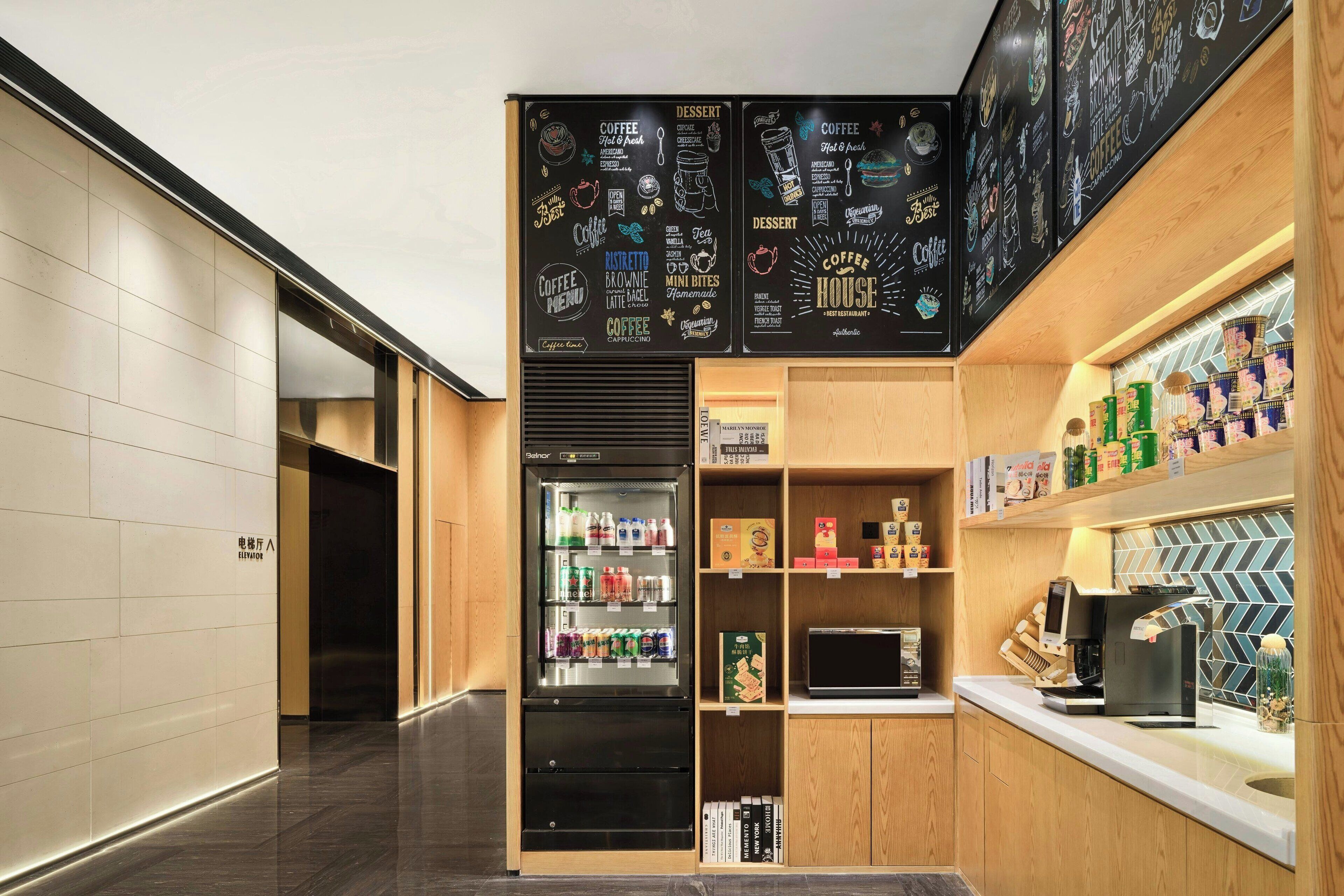 Uma cafeteria moderna com menu em lousa, geladeira repleta de bebidas e uma máquina de café no balcão.