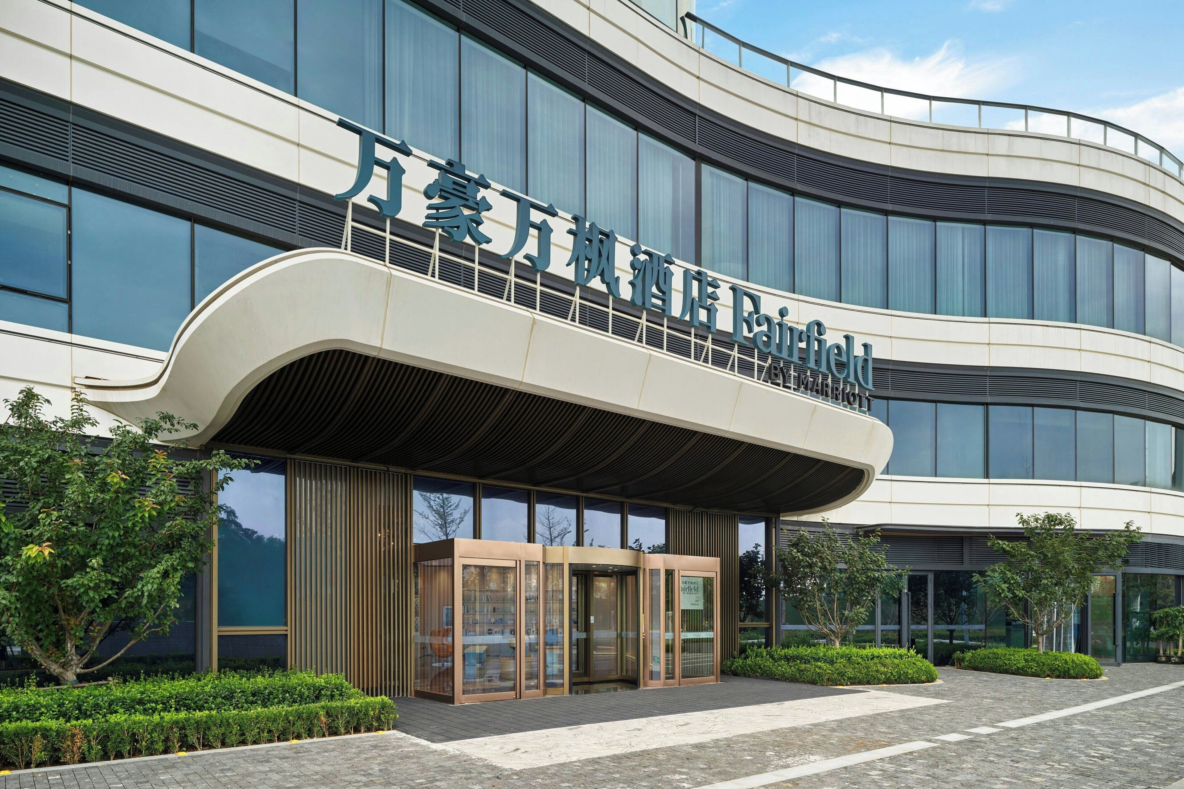 A modern hotel entrance with a curved facade, large glass windows, and a covered entrance area.