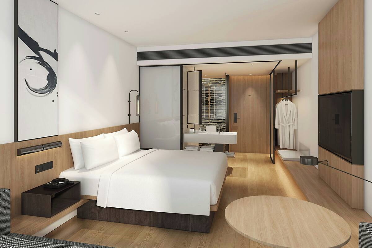 Ein modernes Hotelzimmer mit einem großen Bett, einem runden Tisch, einem Fernseher und einem Badezimmer mit Spiegel und Waschbecken.