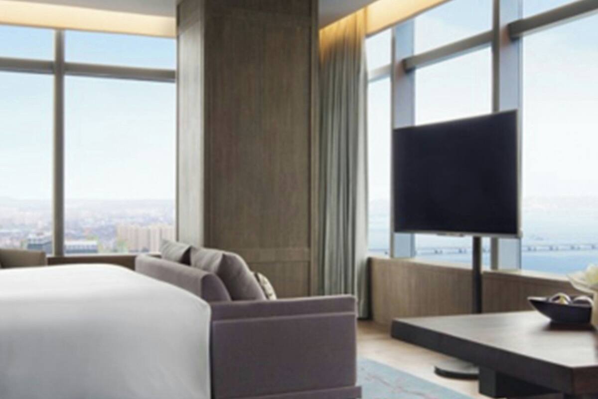 Ein modernes Hotelzimmer mit einem großen Bett, einem Flachbildfernseher und Blick auf die Stadt durch große Fenster.