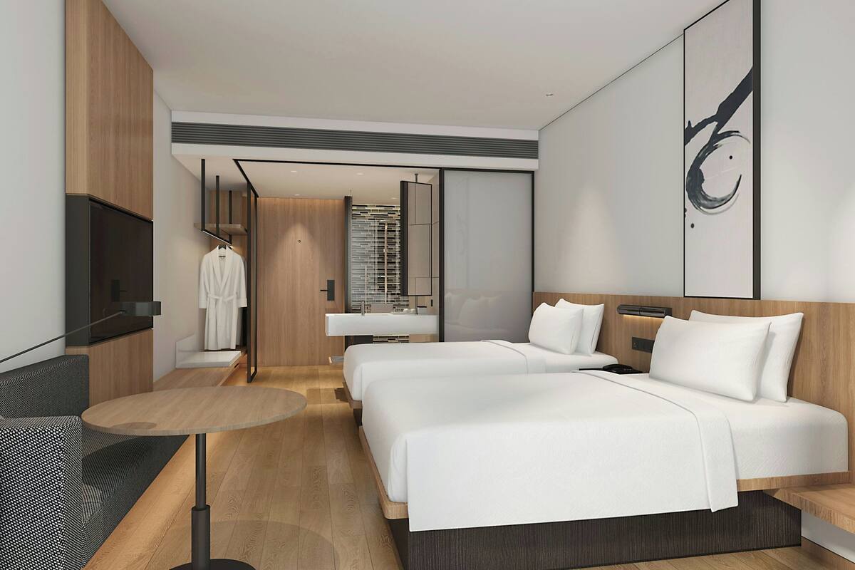 Ein modernes Hotelzimmer mit zwei Betten, einem Fernseher, einem Schreibtisch und einem durch eine geöffnete Tür einsehbaren Badezimmer.