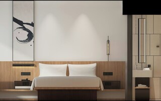 A modern bedroom with a wooden headboard, a large bed with white linens, a wall-mounted light, and a minimalist decor.