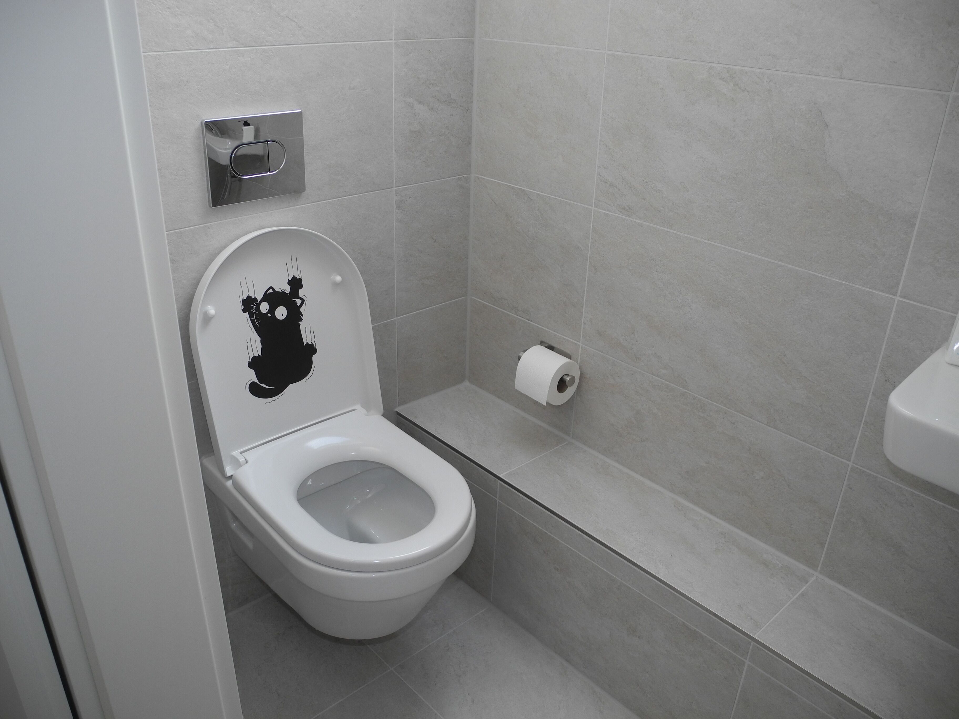 Un baño moderno con inodoro blanco, dispensador de papel higiénico y lavamanos instalado en la pared.
