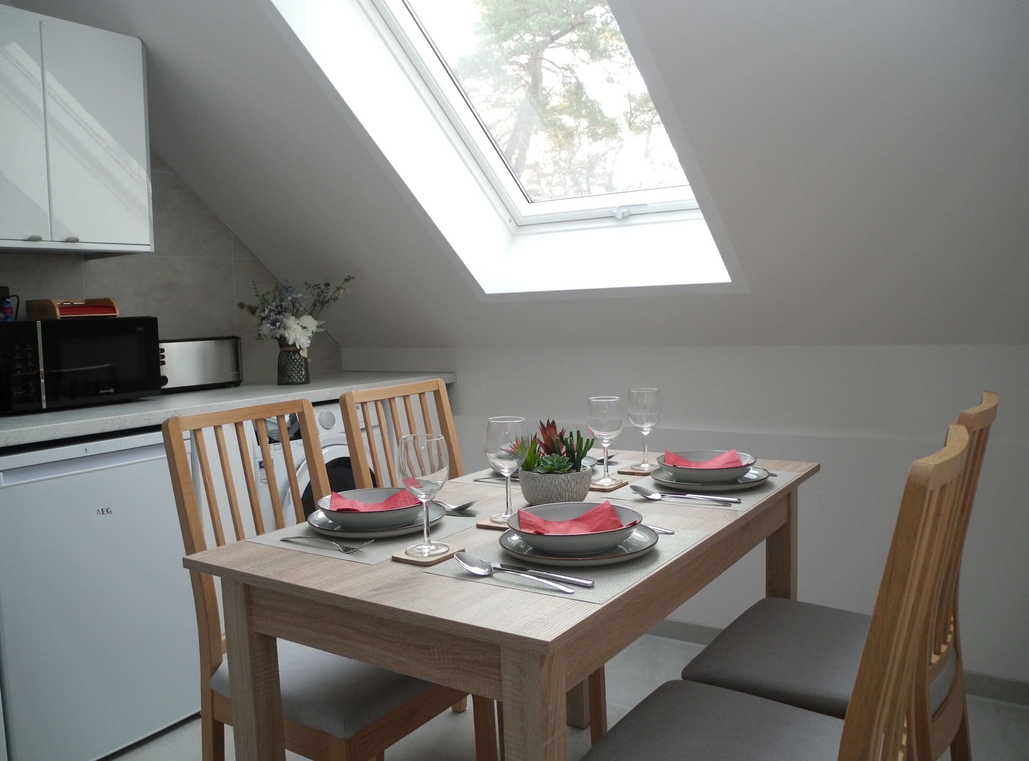 Un coin repas avec une table dressée pour quatre personnes, un four à micro-ondes et un lave-linge en arrière-plan.