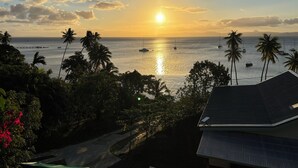 A sunset view over a calm sea with boats, palm trees, and a house with a sloped roof. - A fusion of classic colonial and cool Mediterranean holiday accommodation (Savusavu)