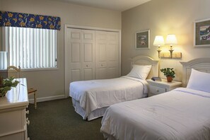 Ein Schlafzimmer mit zwei Einzelbetten, einem Nachttisch mit Lampe, einer Kommode, einem Stuhl und einem Fenster mit Jalousien.