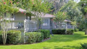 A row of single-story cabins with white railings, surrounded by lush greenery and a well-maintained lawn. - Golden Hour Deck Views + Island Fun Await at This Spacious 3BR Retreat (Hilton Head Island)