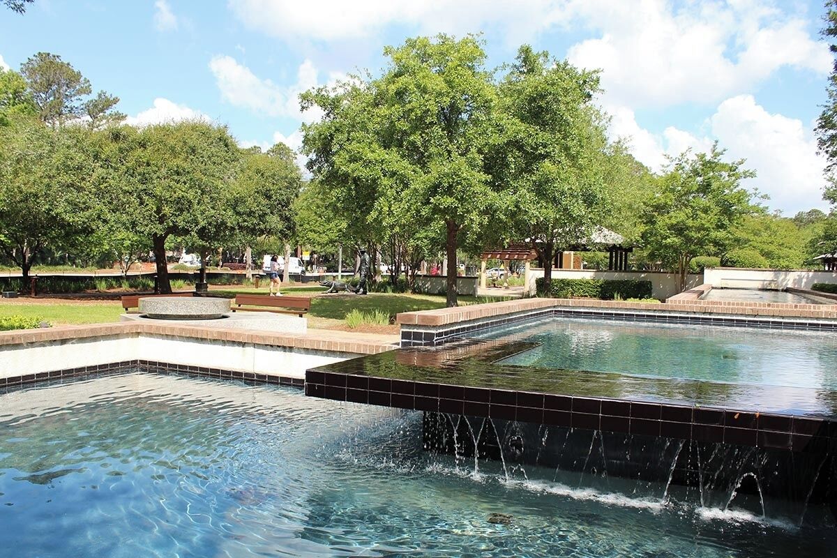 A large rectangular pool with a waterfall feature, surrounded by a landscaped garden with trees and a gazebo.