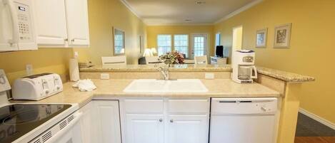 A modern kitchen with white cabinets, a built-in oven, a dishwasher, and a countertop with a sink.