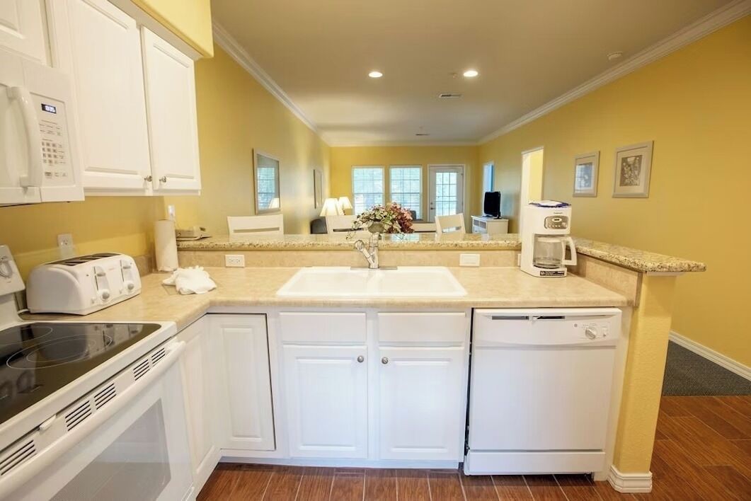 A modern kitchen with white cabinets, a built-in oven, a dishwasher, and a countertop with a sink.