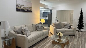 Una sala de estar moderna con un sofá color beige, una mesa de centro de vidrio y una mesita auxiliar.