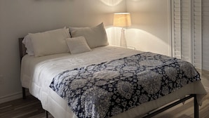 Una cama bien hecha con un edredón estampado, una lámpara de noche y un cuadro de flores en la pared.