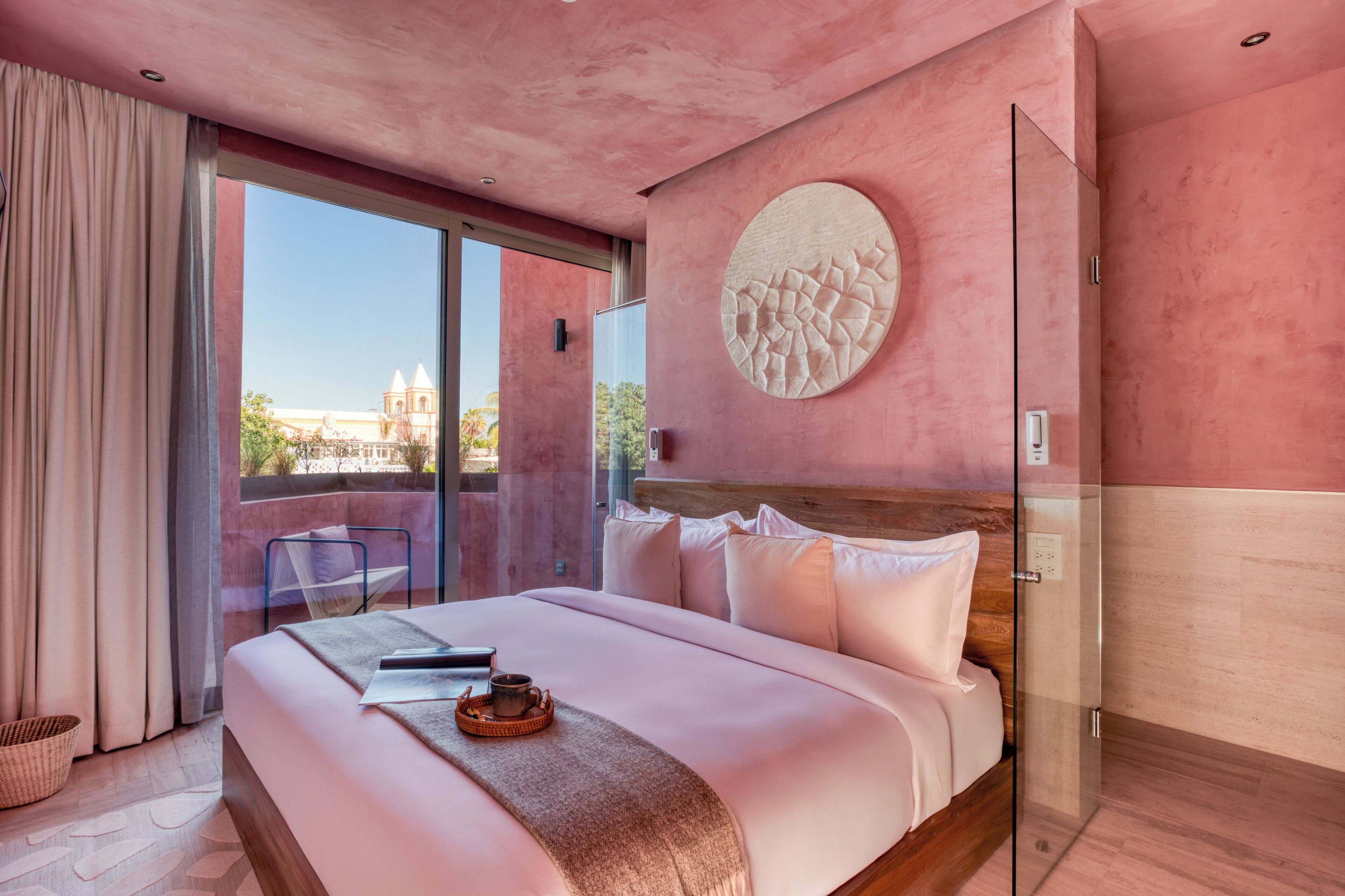 A modern hotel room with a large bed, a glass door leading to a balcony, and a view of a building outside.