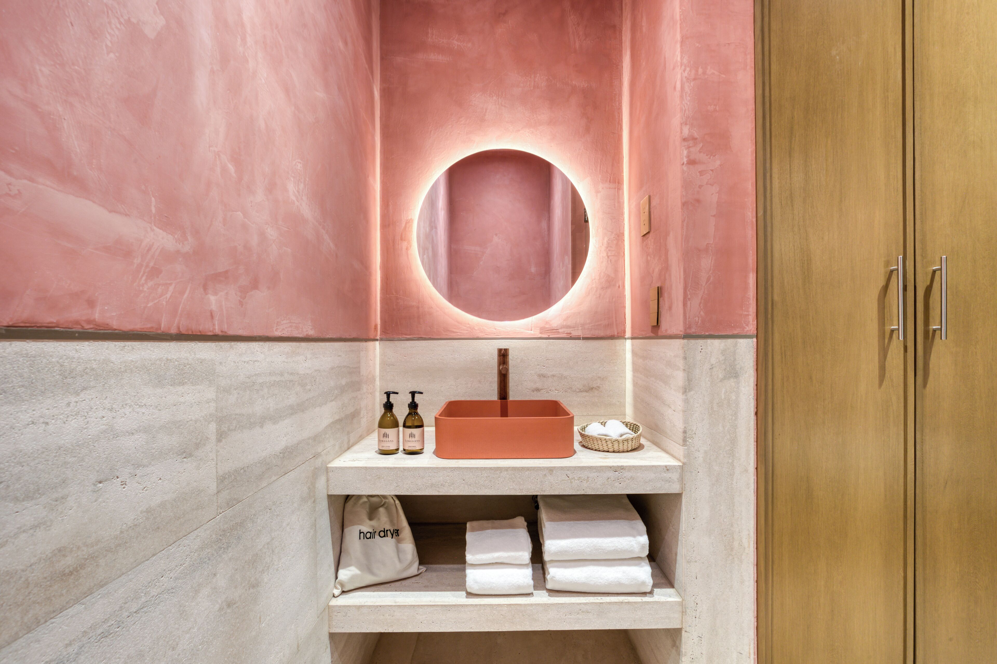 A bathroom with a round mirror, a sink, and a shelf with towels and a hairdryer.