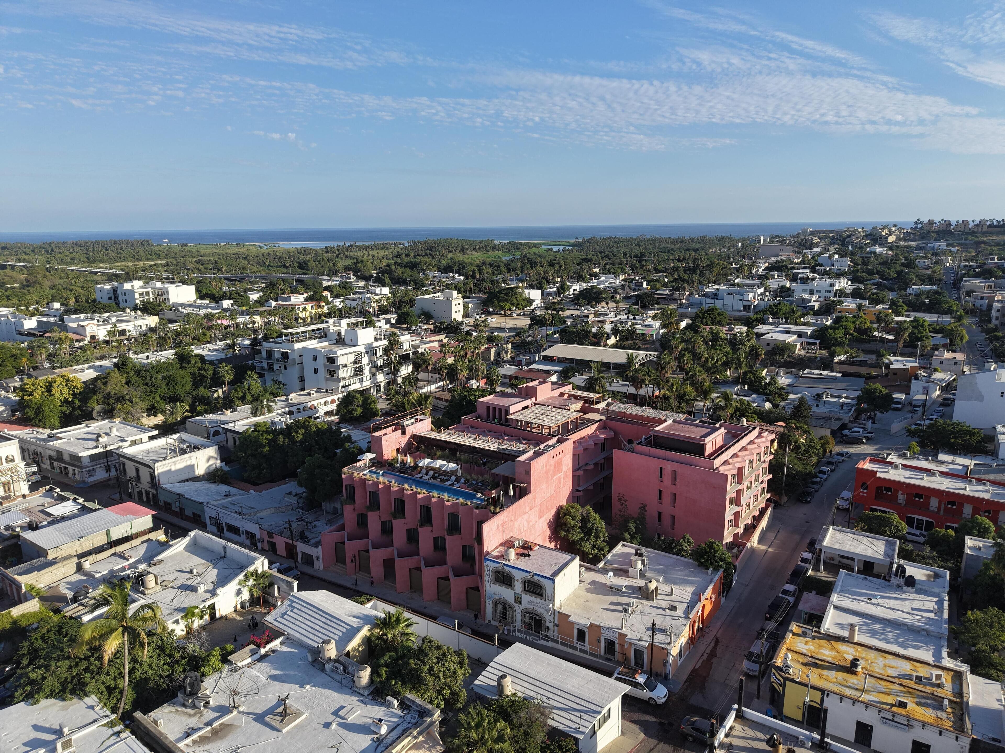 An aerial view of a cityscape with a mix of residential and commercial buildings, including a prominent pink building with a rooftop pool.