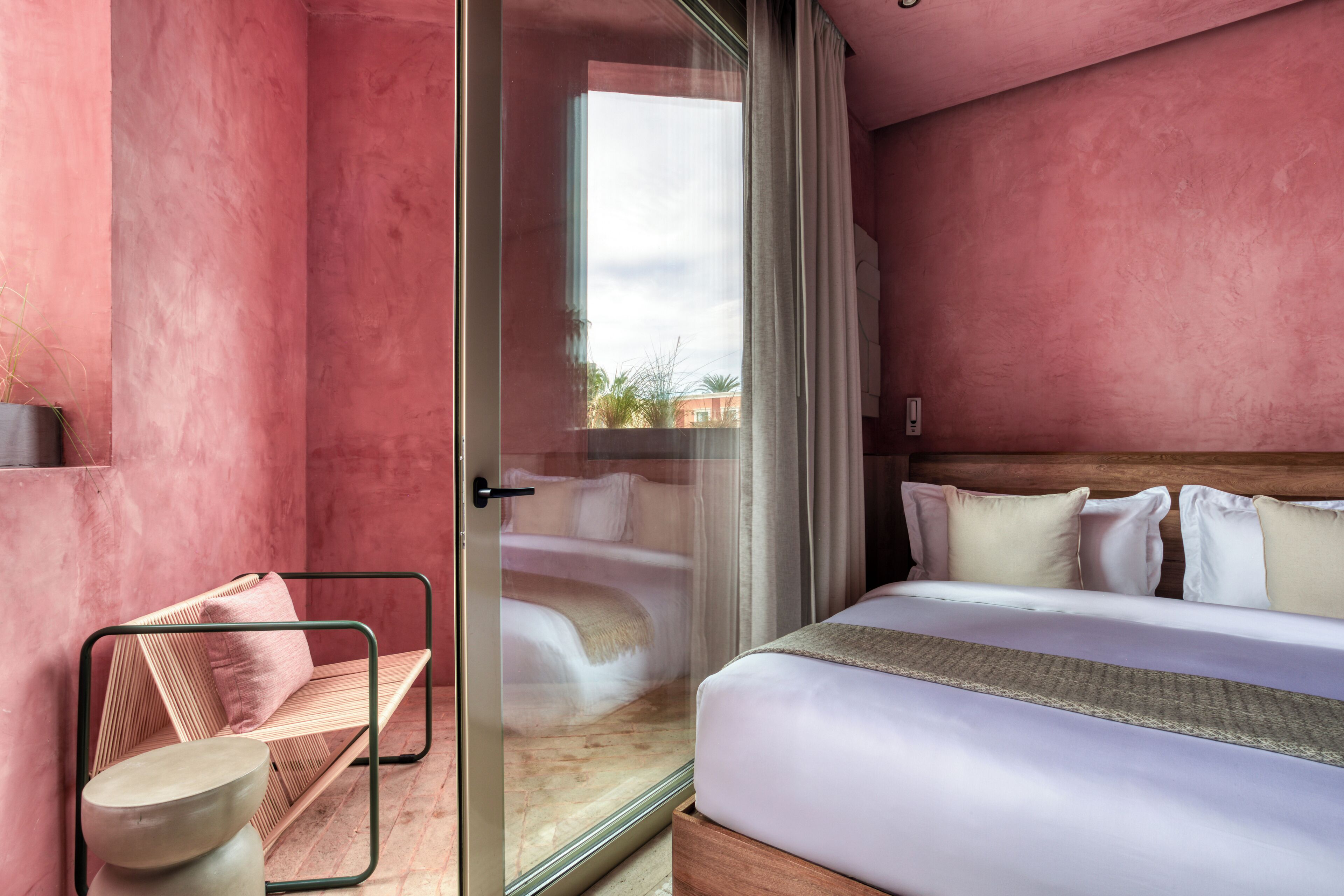 Een slaapkamer met een bed, een bankje en een glazen deur naar een balkon.