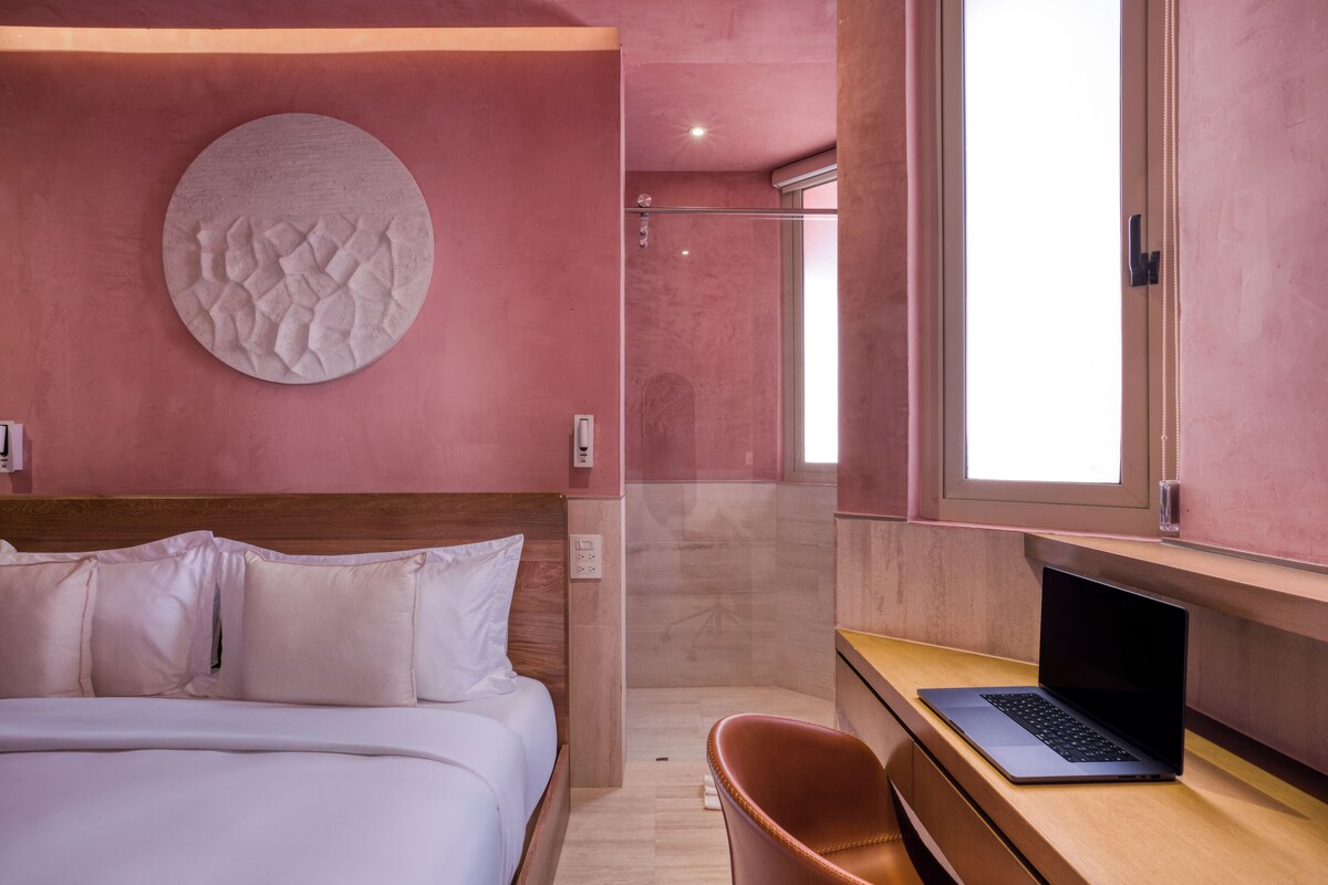 A modern hotel room with a bed, a laptop on a desk, and a shower area.