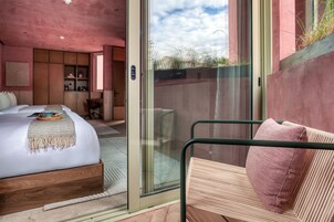 Un dormitorio con cama, una silla y una puerta corrediza de vidrio que da a un espacio exterior.