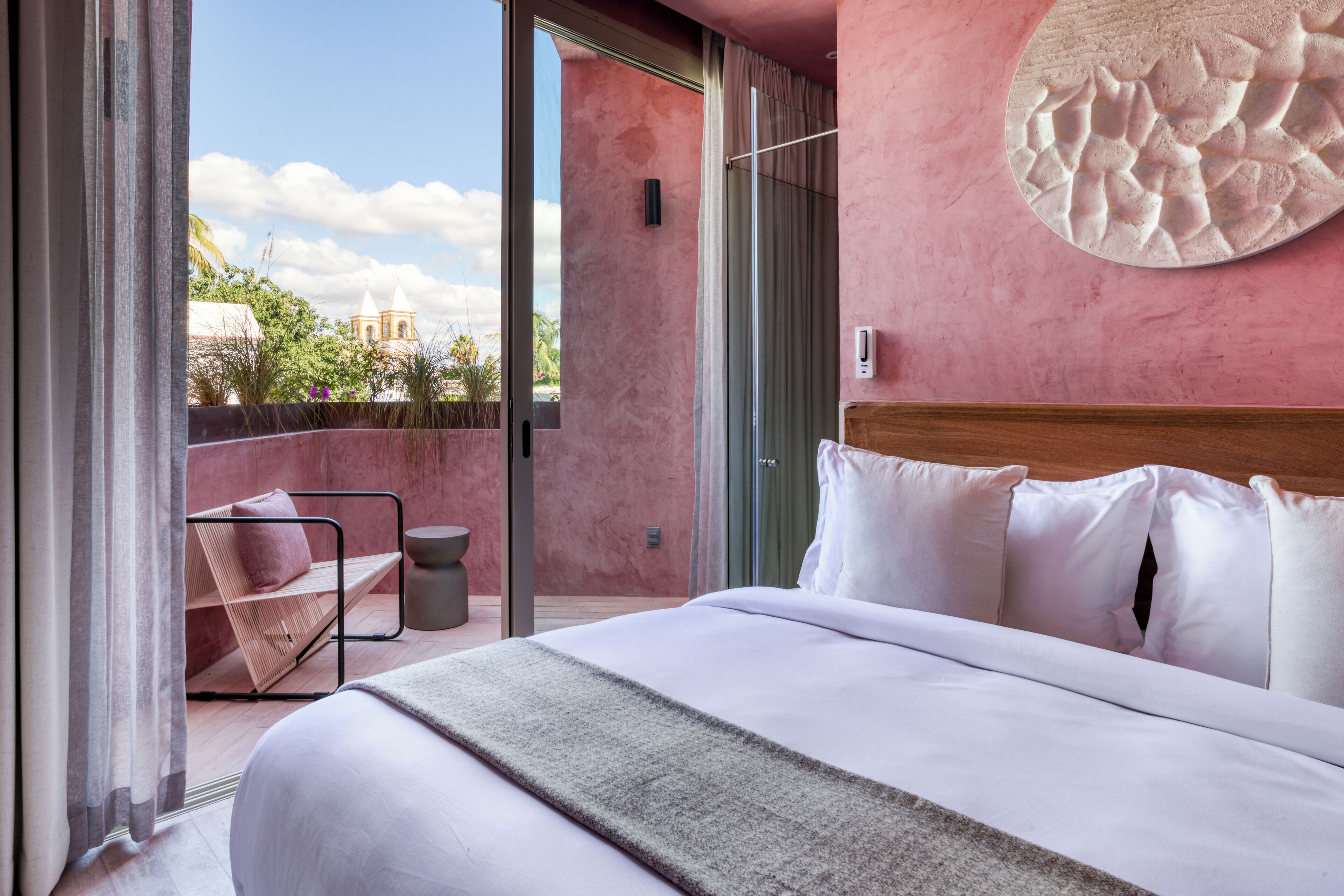 Habitación de hotel moderna con una cama grande, vista a un edificio con una torre, y un balcón con una silla y una mesita.