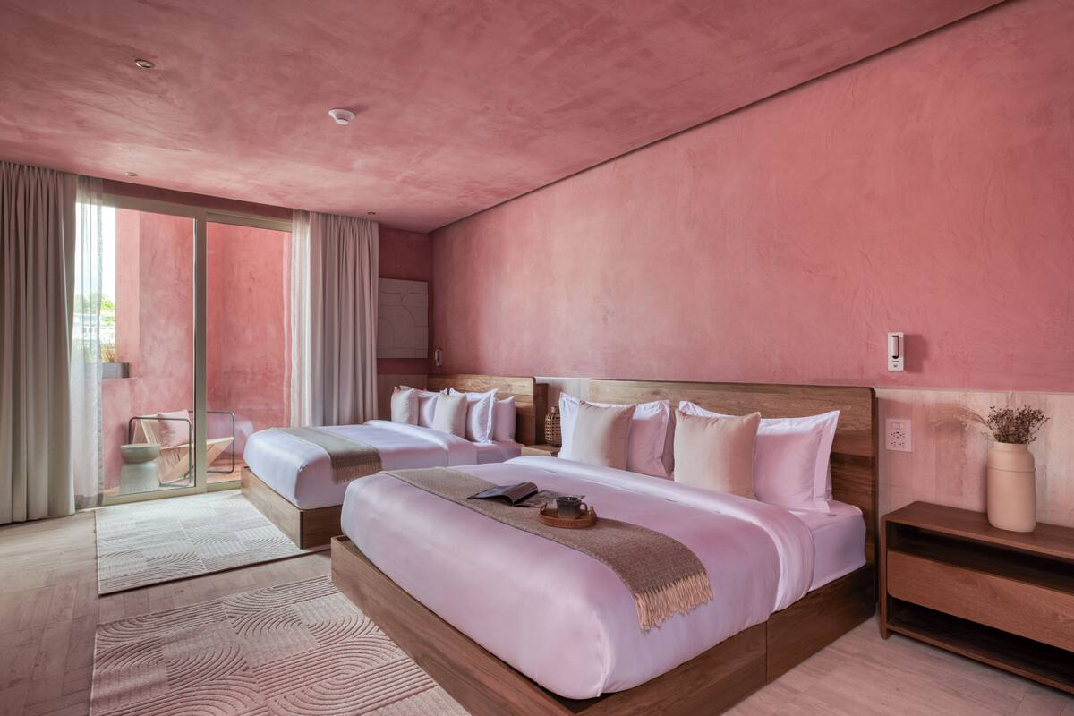 Een moderne hotelkamer met twee bedden, een grote schuifglazen deur naar een balkon en een houten nachtkastje met een vaas.