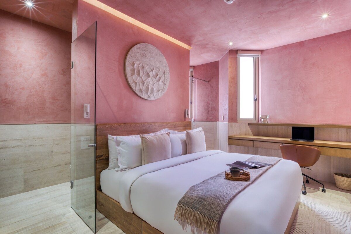 Un dormitorio moderno con una cama grande, un escritorio y un box de ducha de vidrio.