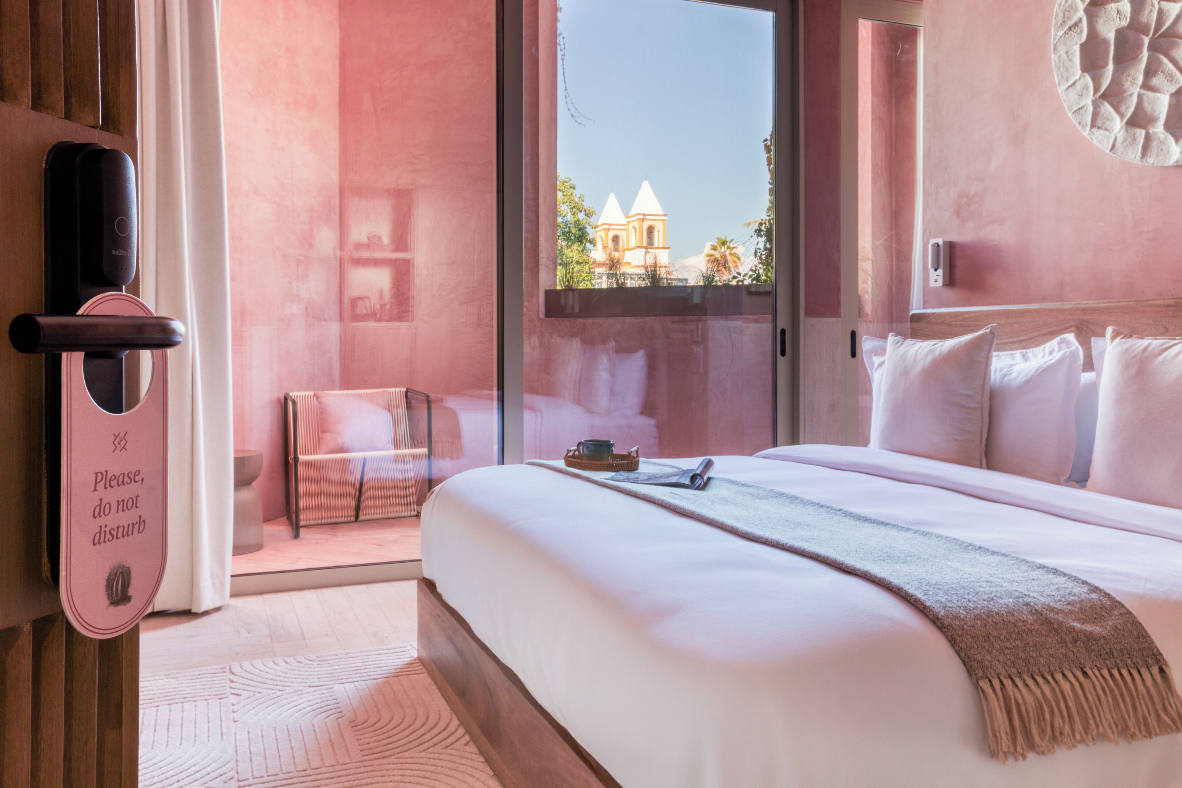 Habitación de hotel con una cama grande, vista de una iglesia a través de la ventana y una puerta con un cartel de 'No molestar'.