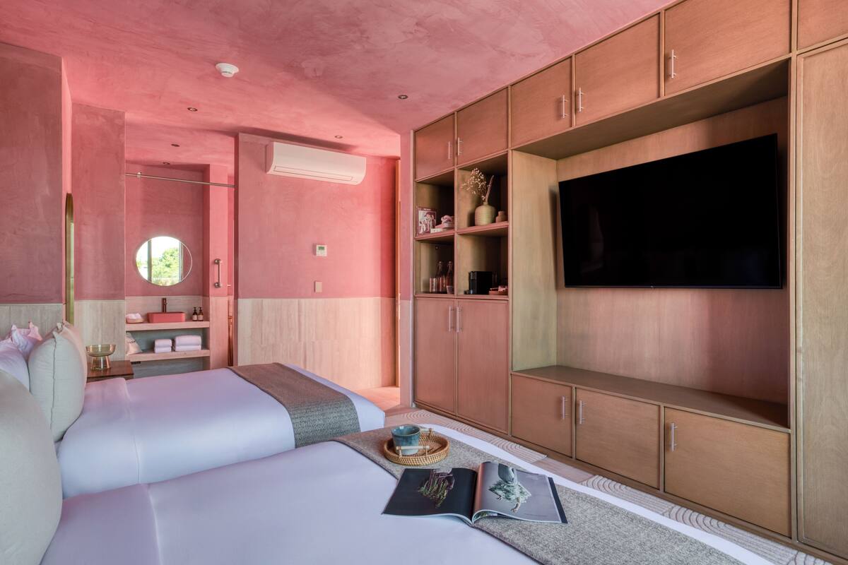 Een slaapkamer met twee bedden, een televisie, houten kasten en een kleine badkamer.