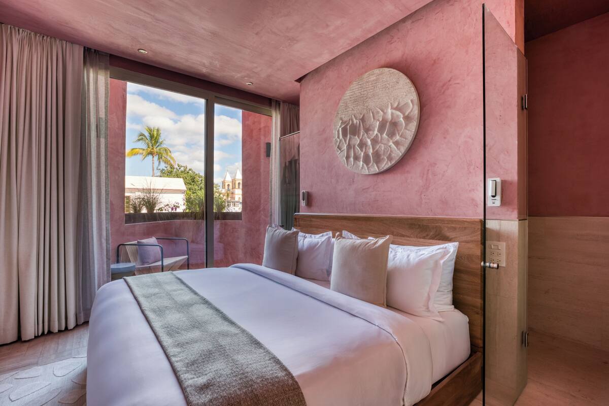 Een hotelkamer met een groot bed, een ronde wandversiering en uitzicht op palmbomen en een gebouw.