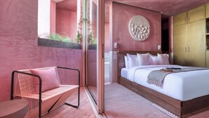 Un dormitorio moderno con una cama grande, un sillón y vistas a la vegetación a través de una puerta corredera.