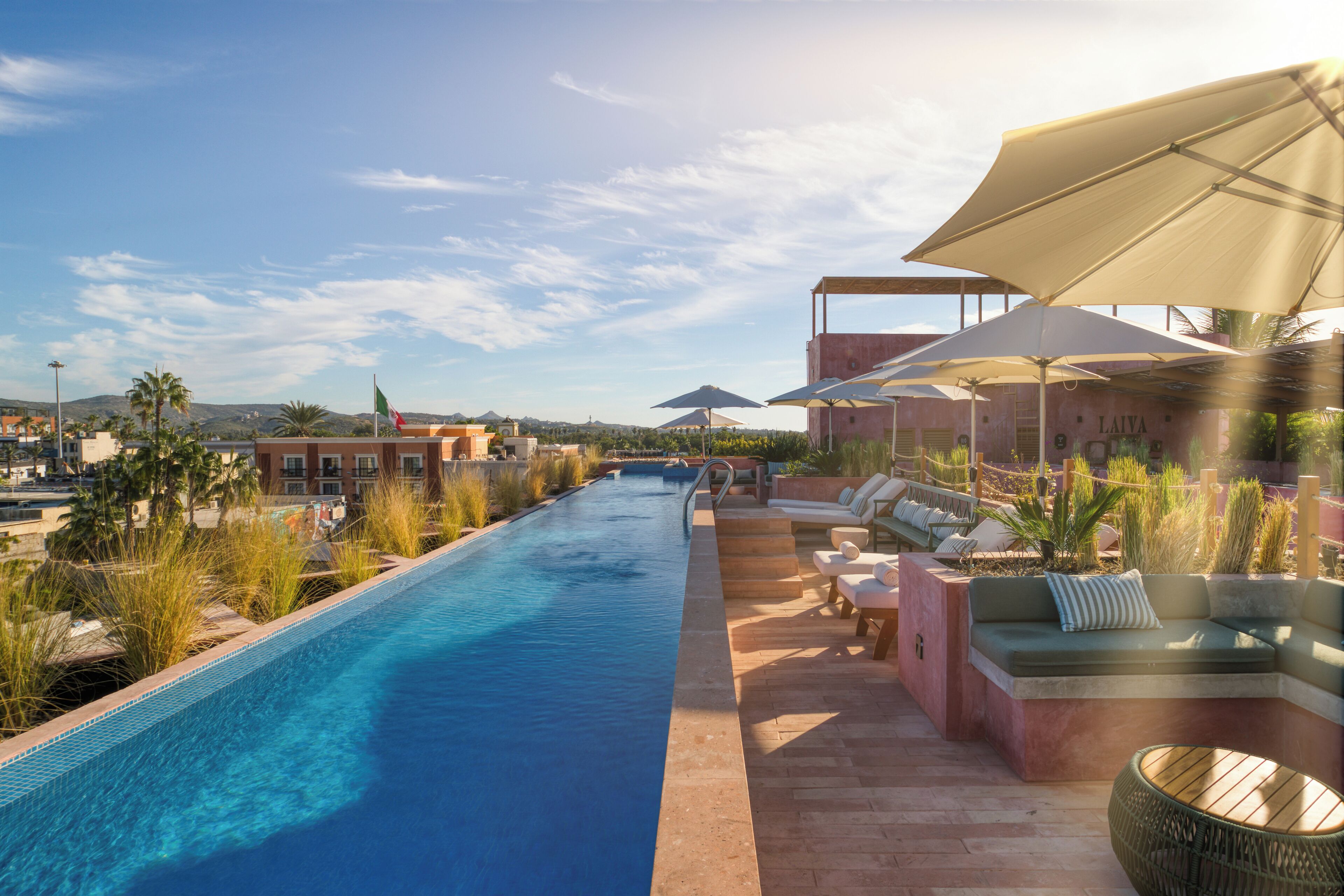 A poolside area with a long swimming pool, lounge chairs, and umbrellas.