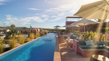 A poolside area with a long swimming pool, lounge chairs, and umbrellas.