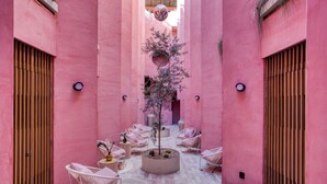 Un patio con paredes rosadas, sillas de mimbre y un macetero central con un árbol.