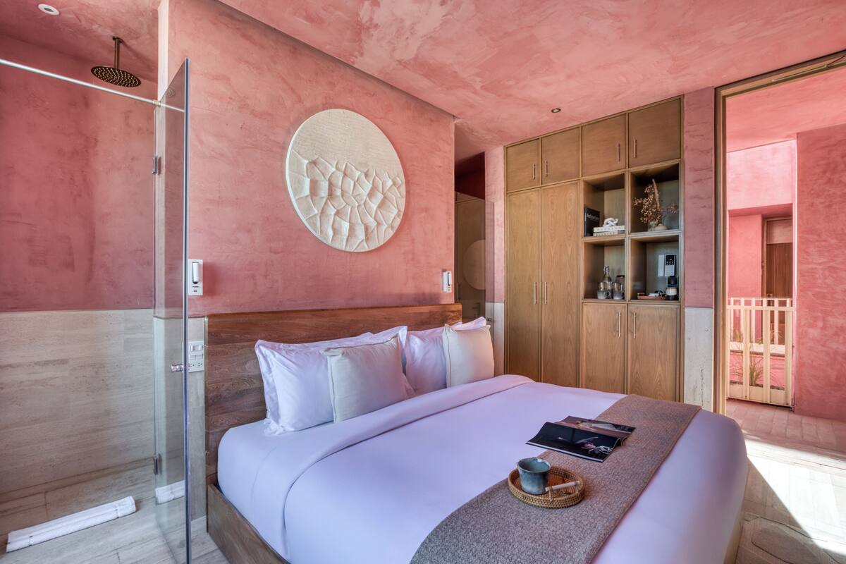 Een moderne slaapkamer met een groot bed, een douchecabine van glas, een houten garderobe en een ronde wanddecoratie.