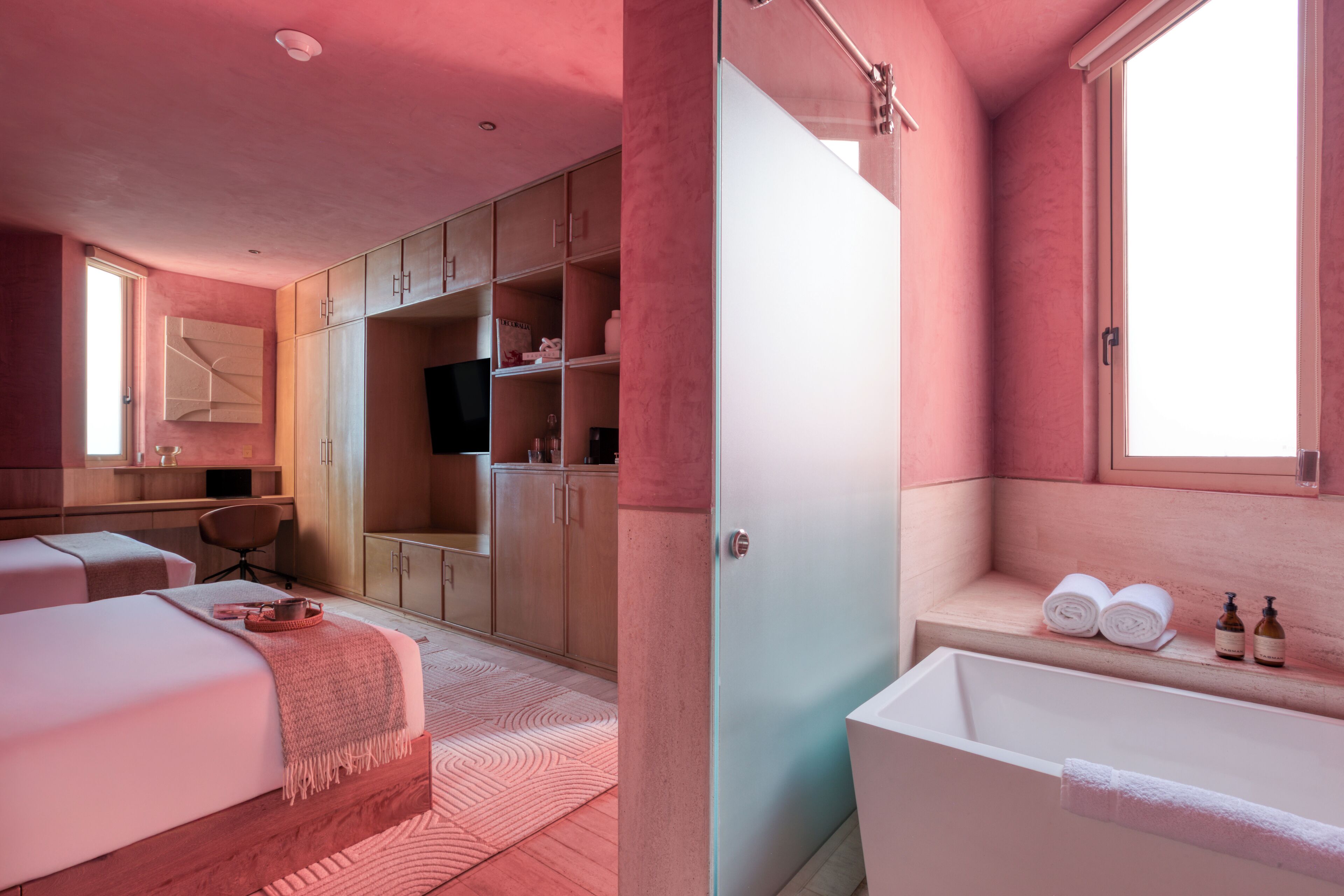 A modern bedroom with a large bed, a walk-in closet, a desk, and a bathroom with a bathtub and towels.