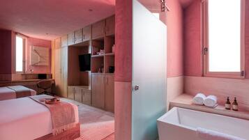 A modern bedroom with a large bed, a walk-in closet, a desk, and a bathroom with a bathtub and towels.