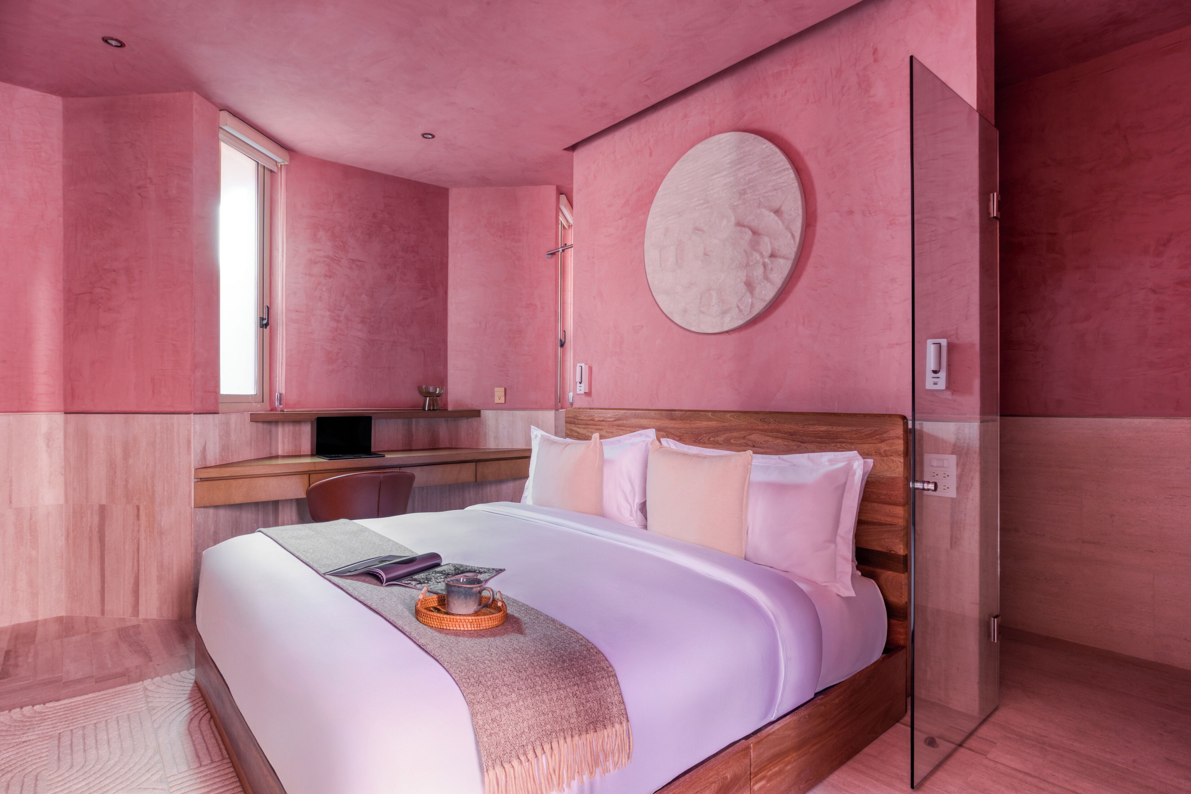 Ein modernes Schlafzimmer mit einem großen Bett, einem Nachttisch, einer runden Wanddekoration und einer Glastür zu einem anderen Raum.