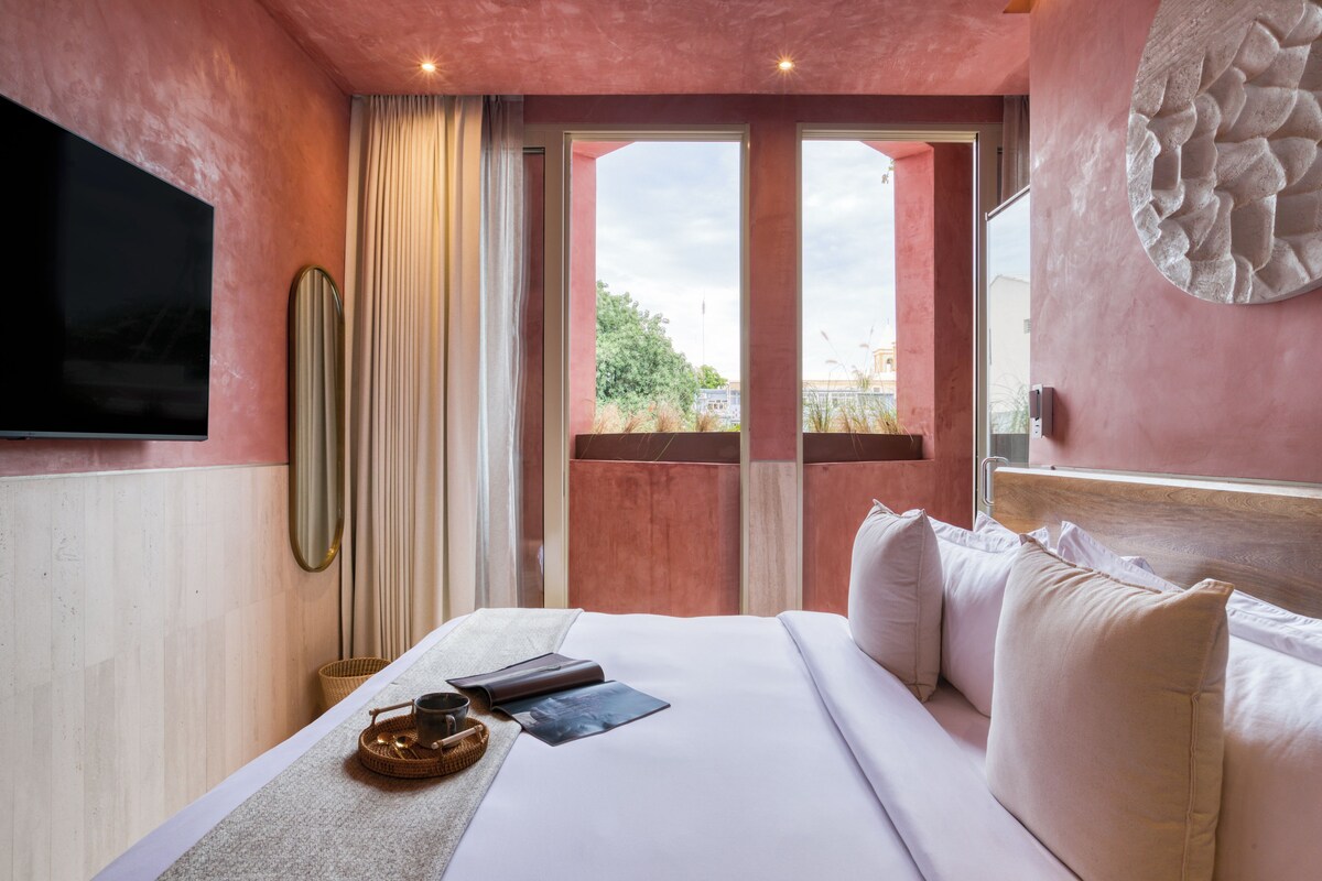 Habitación de hotel con una cama grande, televisión de pantalla plana, espejo y vistas al exterior.