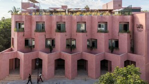 Un edificio rosa con varios balcones y ventanas, que presenta un techo plano con plantas.