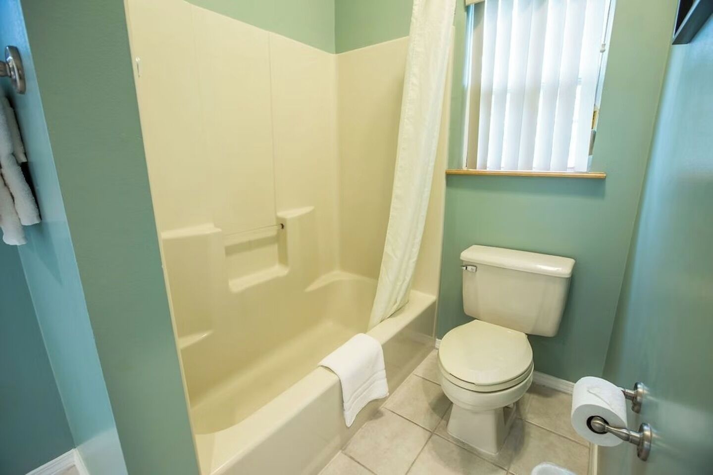 Ein Badezimmer mit Badewanne, Toilette und einem Fenster mit Jalousien.
